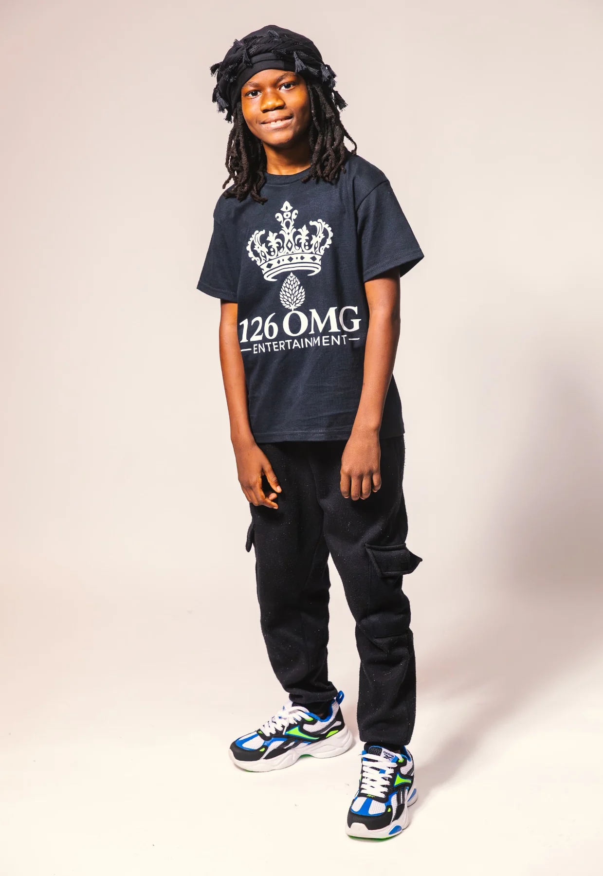 A son in a 126 OMG Entertainment shirt, cargo trousers, and multicolored sneakers